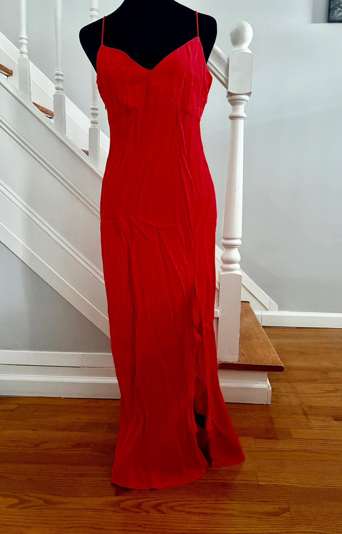 Red long dress with thin straps on a black mannequin, located in front of a wooden staircase and white banister.