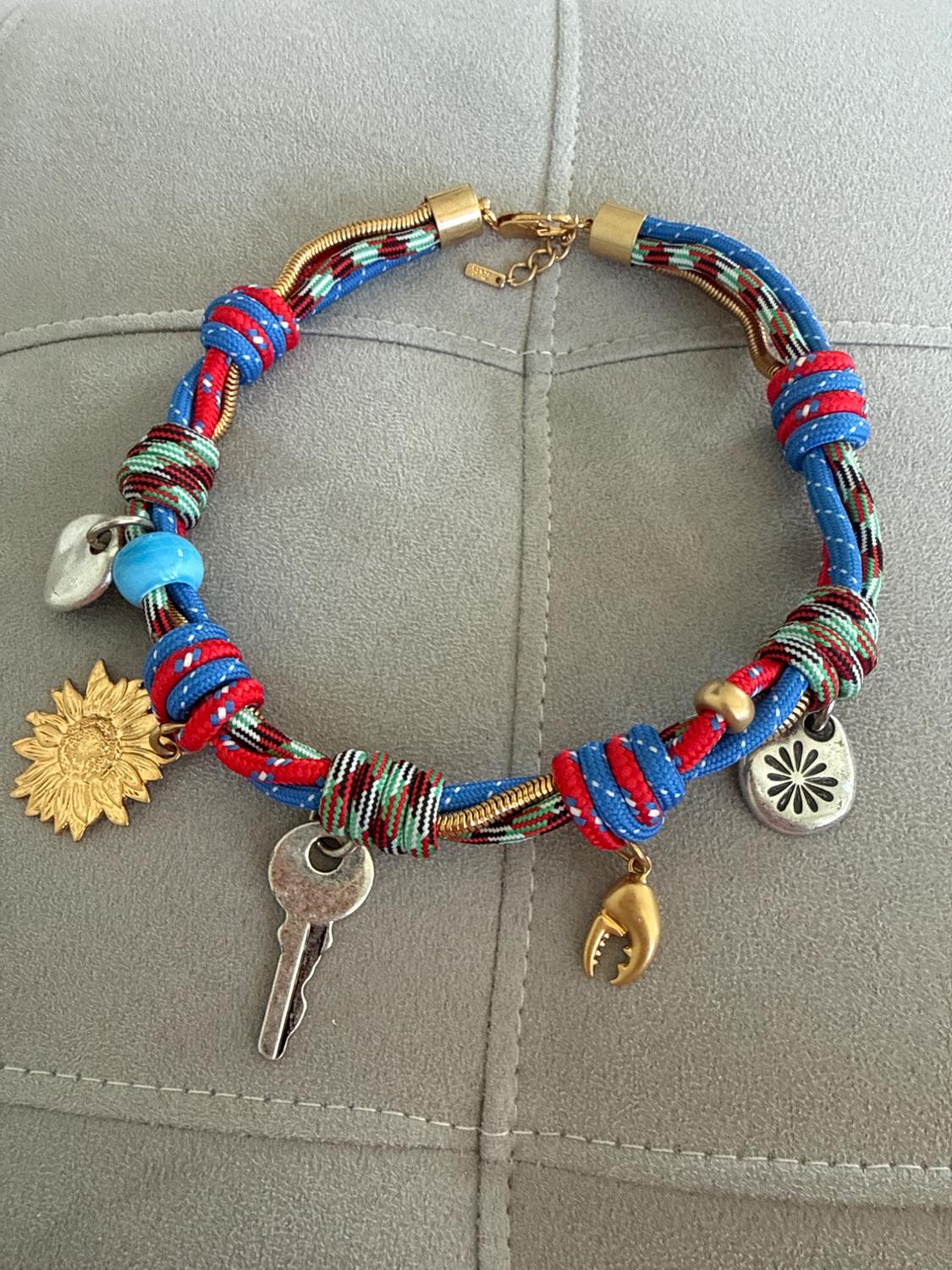 Colourful necklace with knots and key, claw, sunflower, and bead pendants on a light grey background.