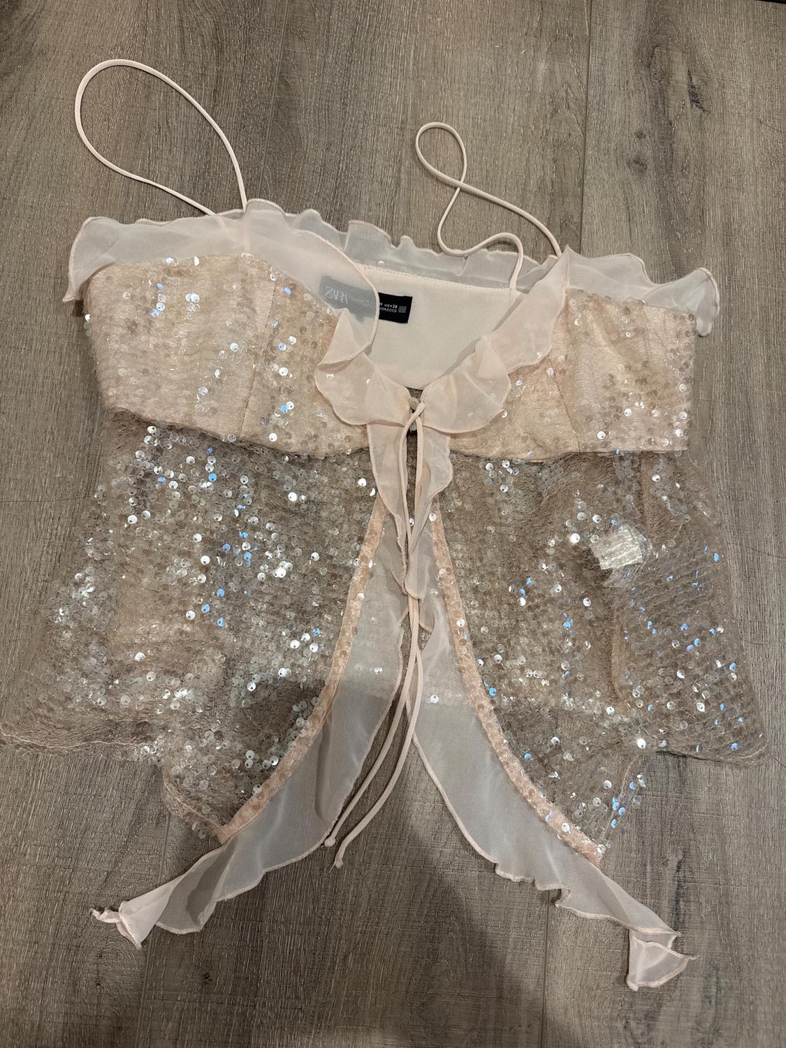 Silver sequin camisole with chiffon ruffles on a wooden background. Visible tag with "ZARA" text.