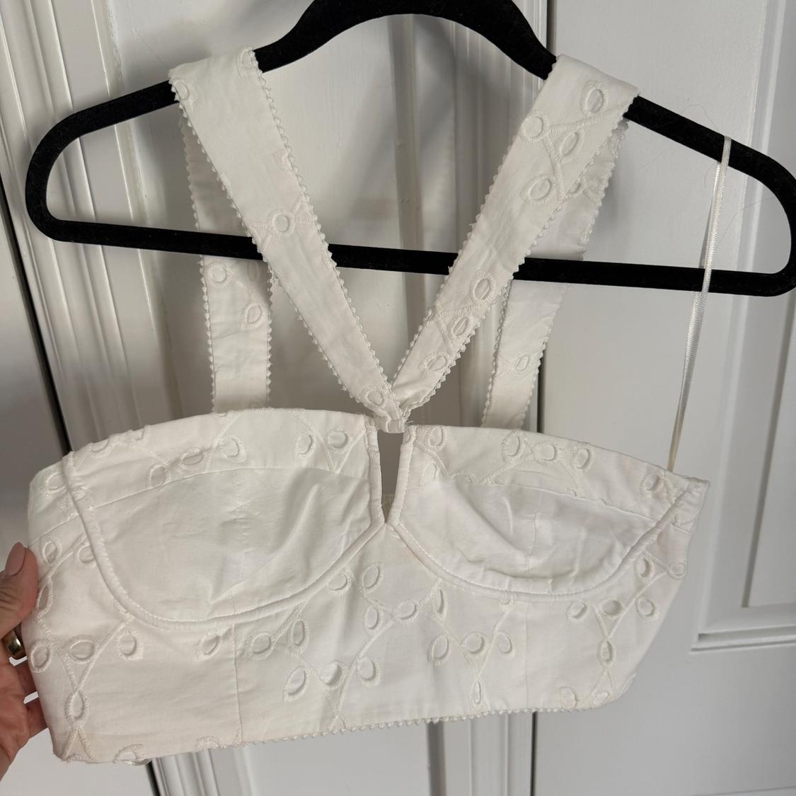 White top with wide straps and floral embroidery hanging on a black hanger in front of a white door.
