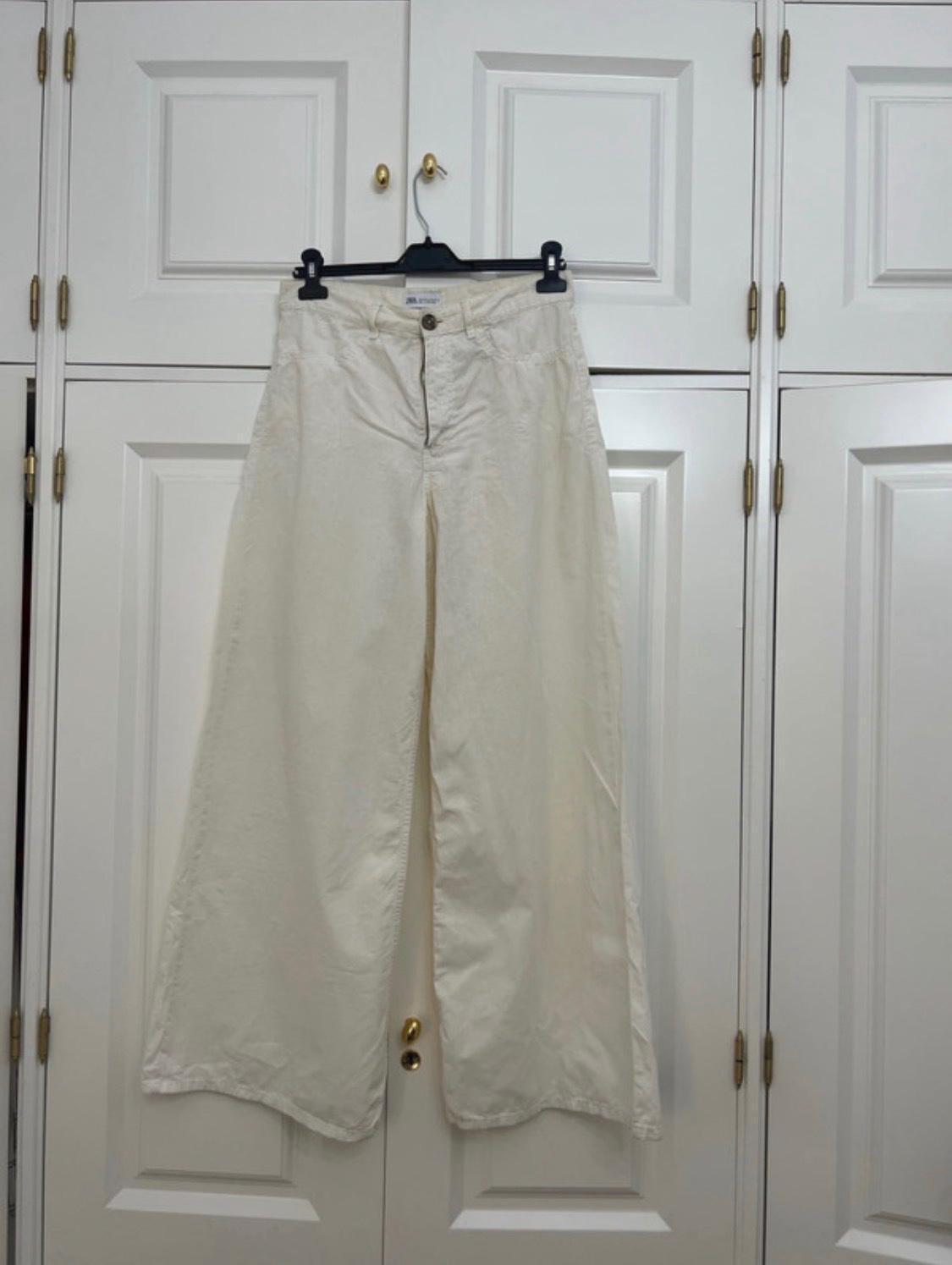 White wide-leg trousers hanging on a black hanger over the doors of a white wardrobe. Casual and relaxed style.