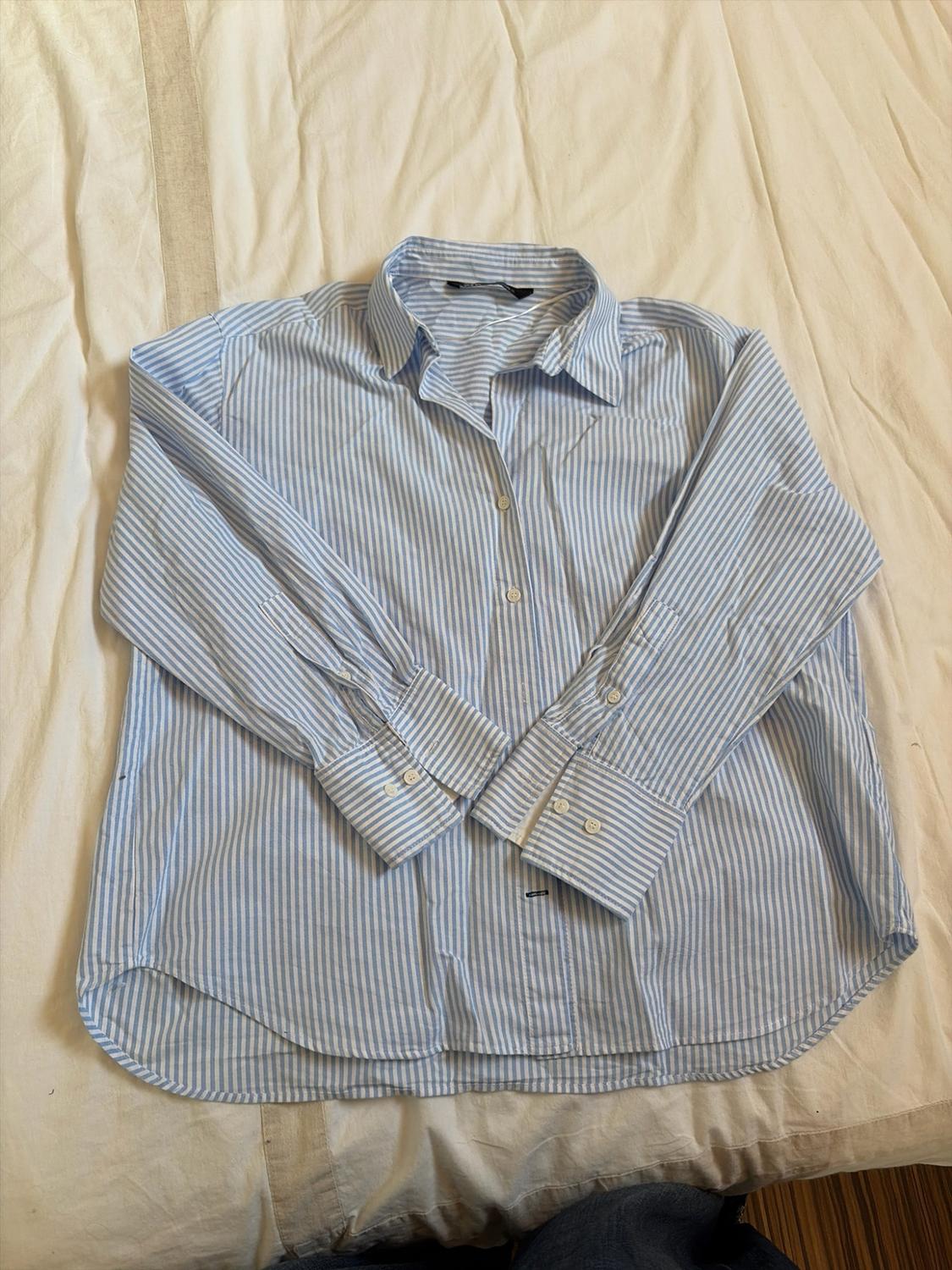 Blue and white striped long-sleeved shirt, with the sleeves crossed at the front, laid out on a crumpled white sheet.