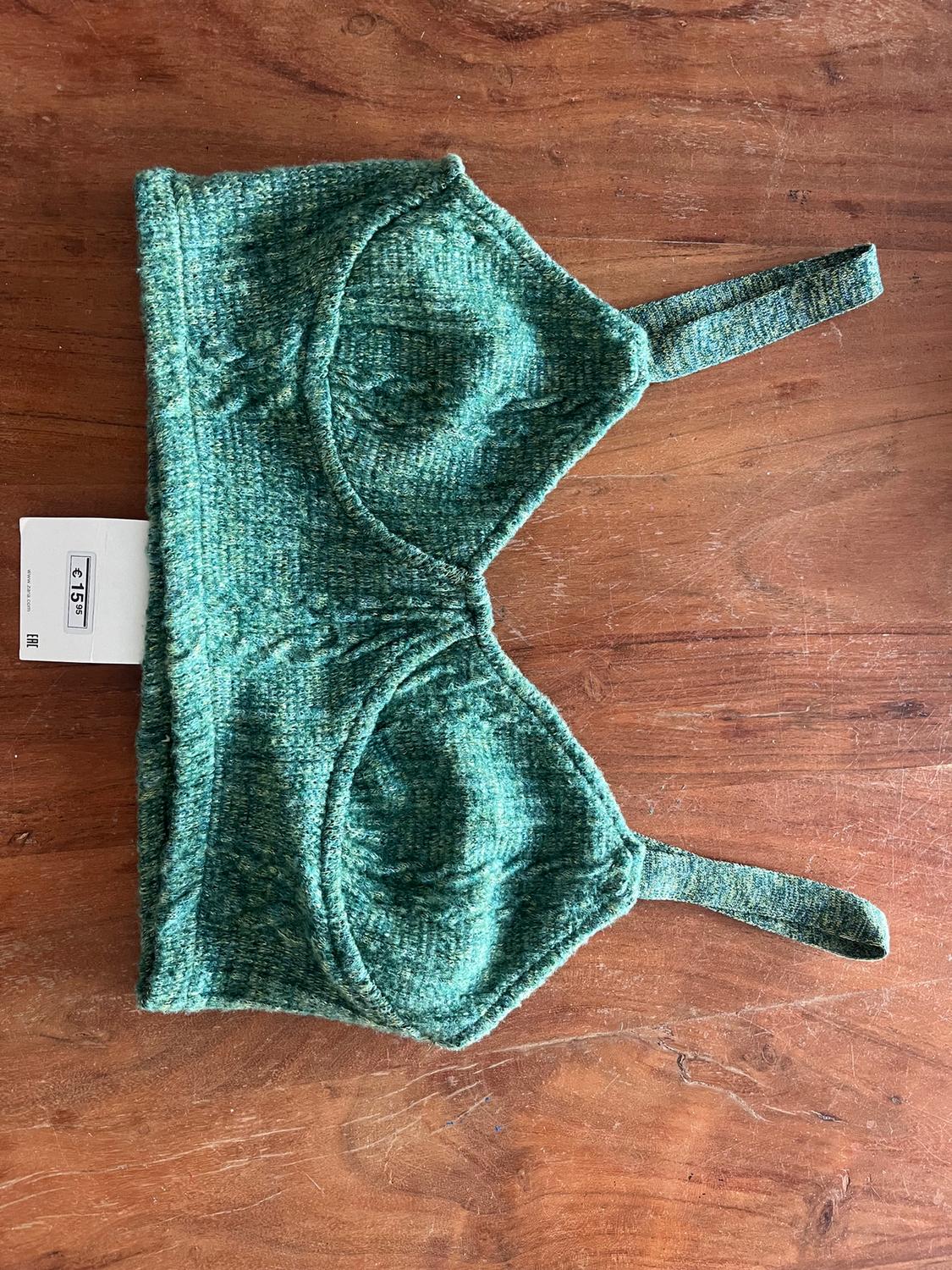 Green knitted bra on a wooden table, with a visible tag indicating a price of 15 euros.