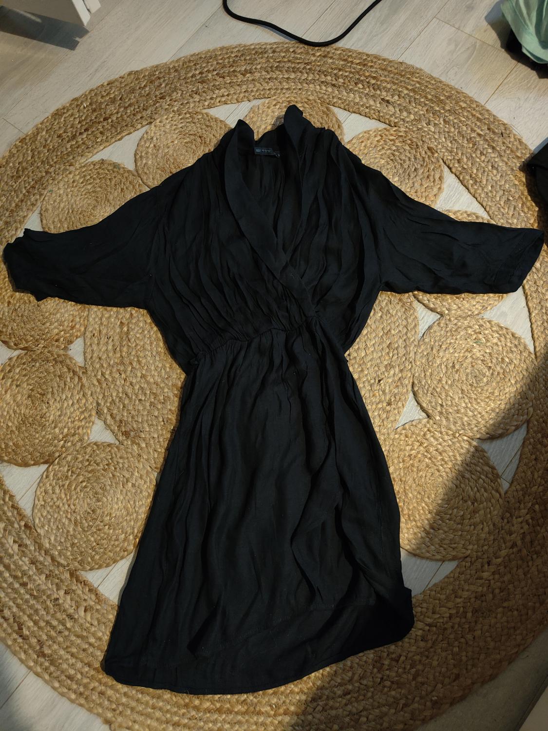 Long-sleeved black dress with a wrap neck, laid out on a round jute rug on a light wood floor.