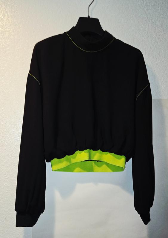 Black long-sleeve sweatshirt with green stitching details and a green elastic band at the hem, hanging on a hanger.