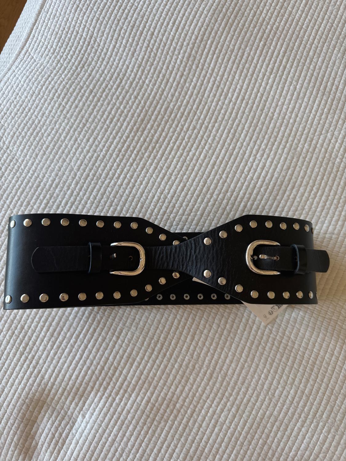 Wide black belt with studs and two silver buckles, on a white ribbed fabric in a relaxed setting.