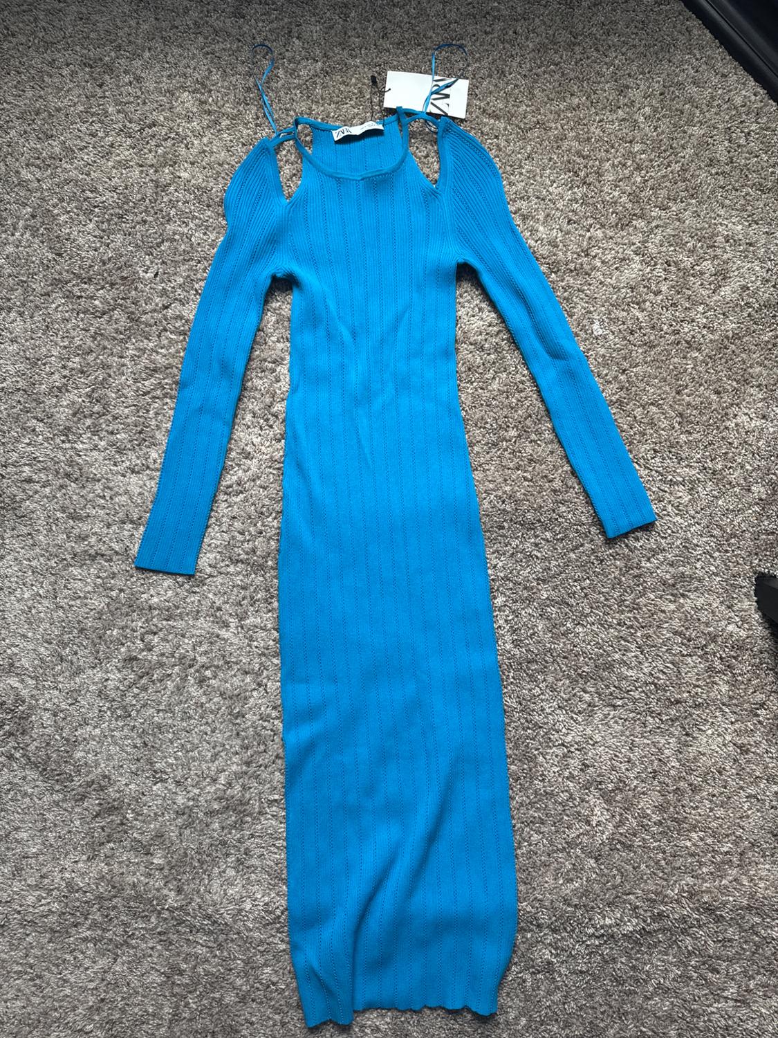 Blue ribbed knit long-sleeve dress with an off-the-shoulder neckline and thin straps, laid on a rug. Label with the text ZARA.