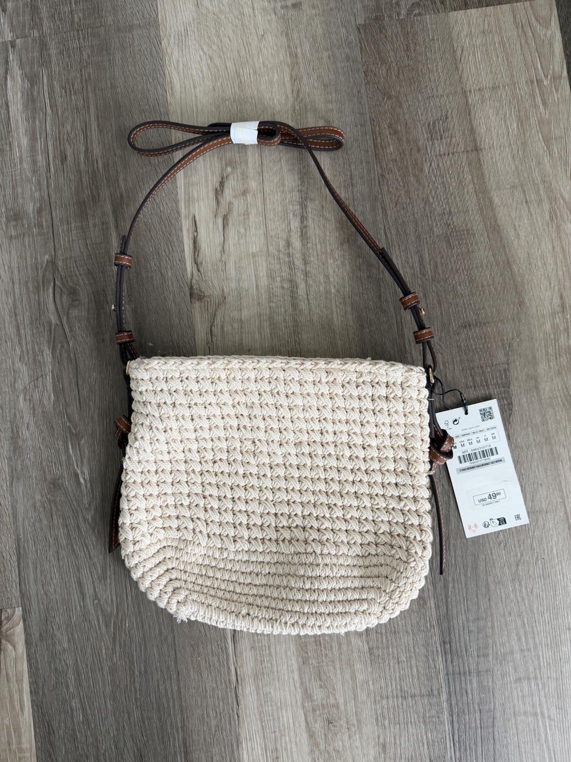 Beige woven bag with brown leather strap on wooden floor. Visible tag with price of 49 USD.