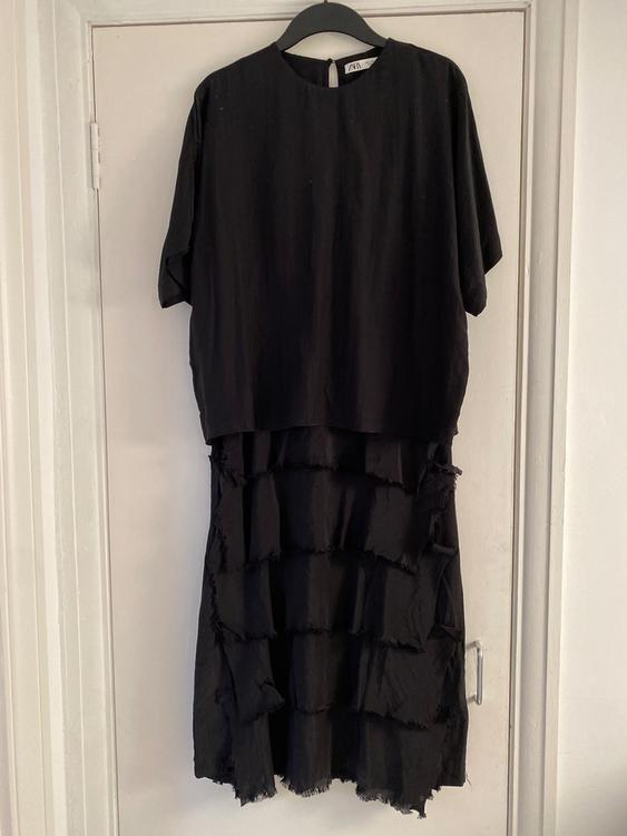 Black short-sleeved dress with layered ruffle skirt, hanging on a hanger over a white door.