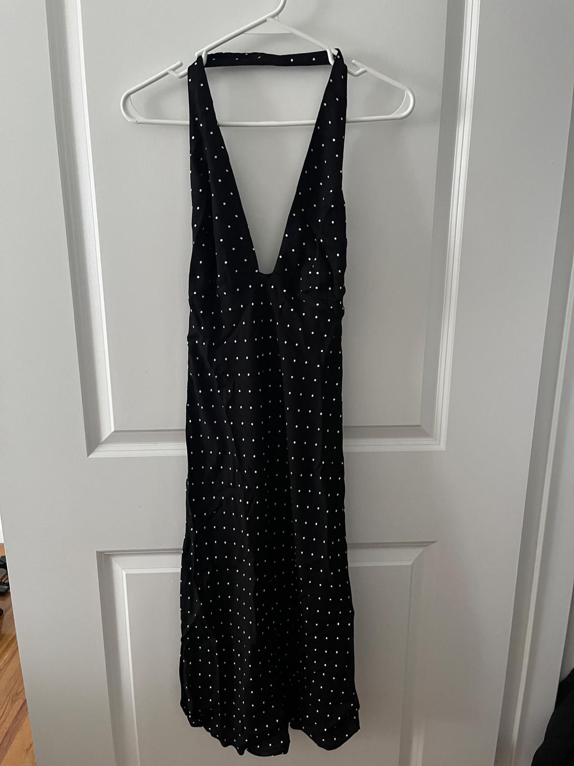 Black dress with white polka dots and a V-neck, hanging on a white hanger over a white door.