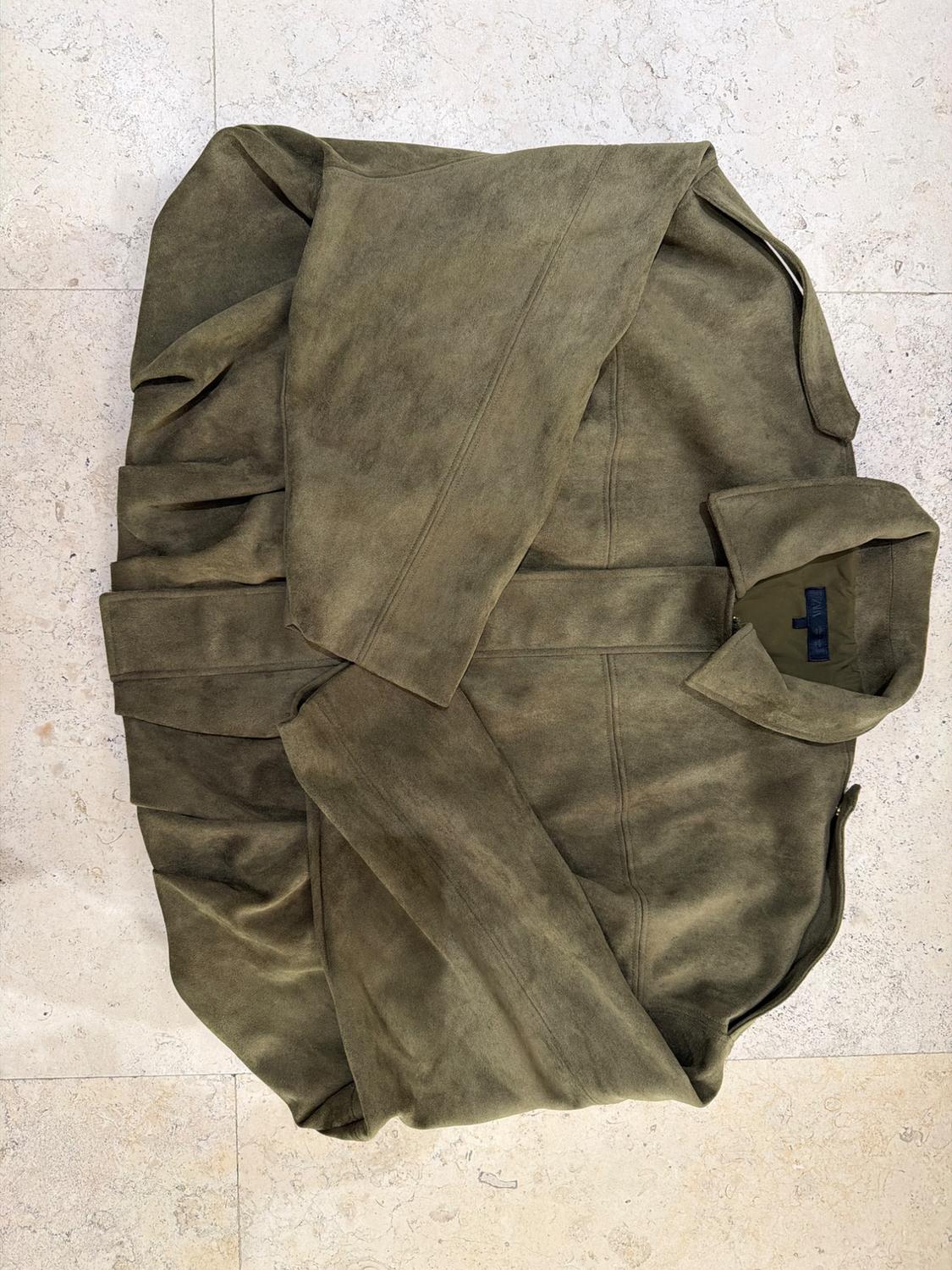 Overhead view of an olive green collared jacket, folded with the sleeves crossed on a light tiled floor.