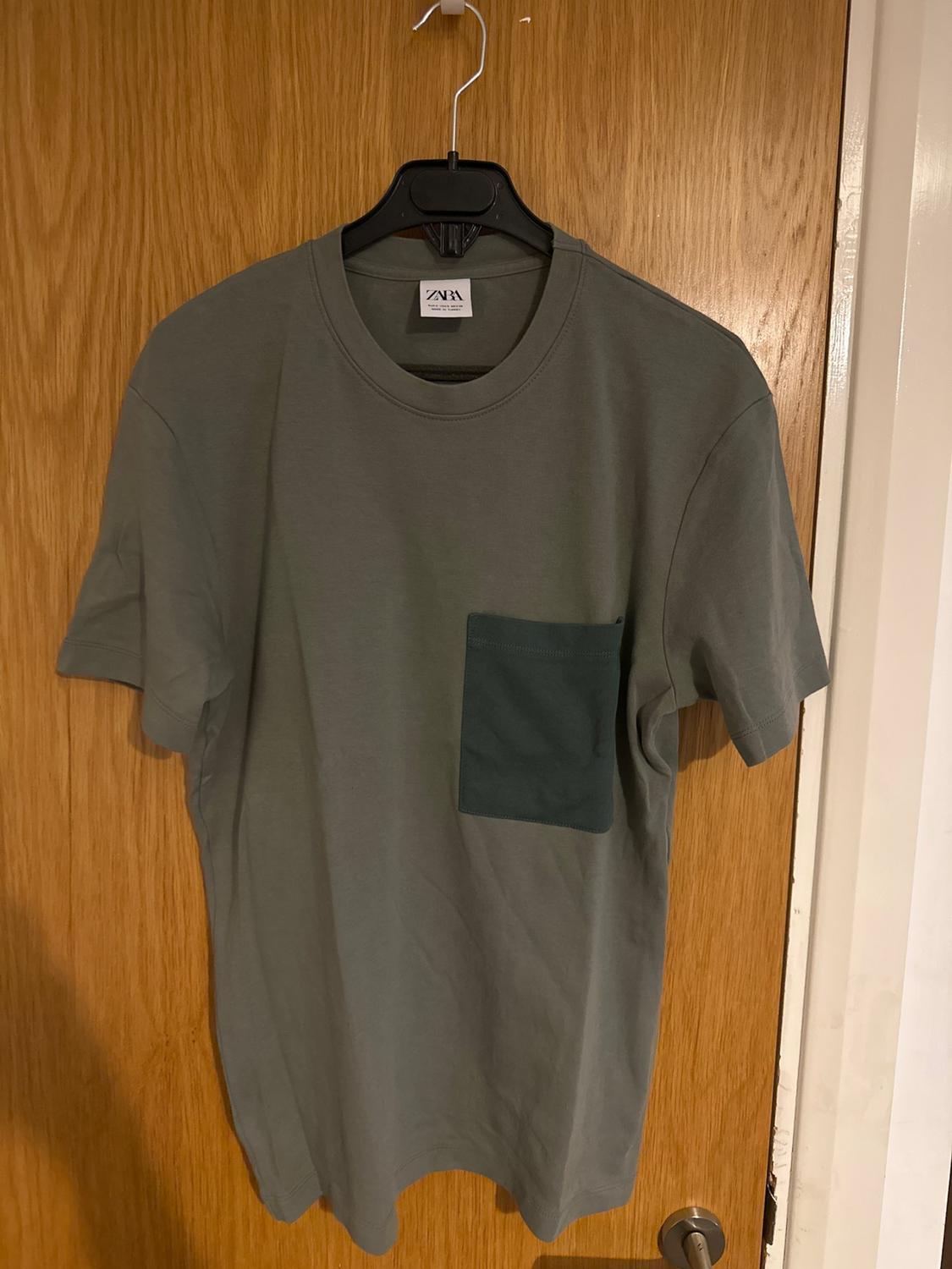 Front view of a grey t-shirt with dark front pocket on a hanger