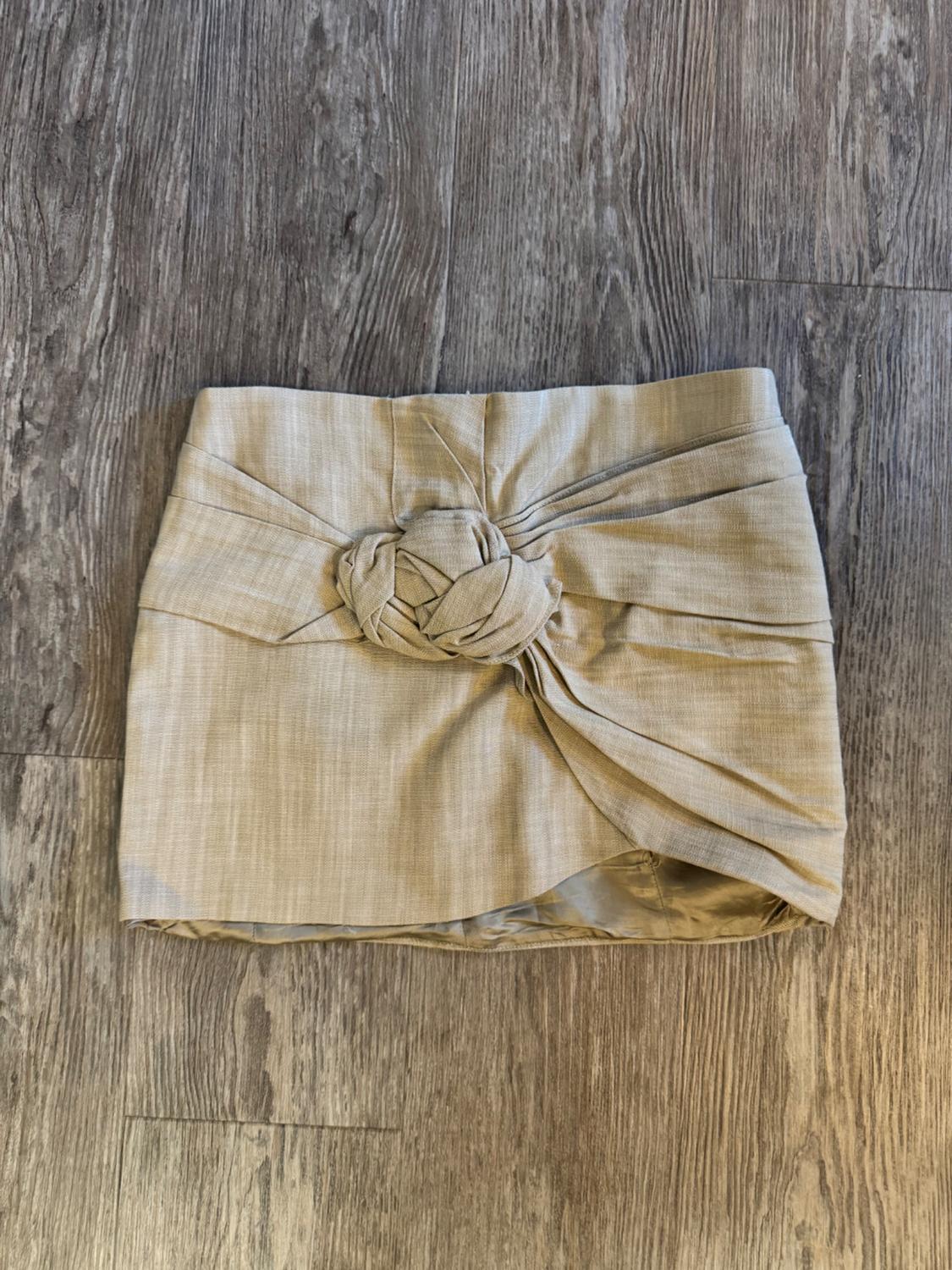 Beige mini skirt with knot detail at the front, on a grey wooden floor.