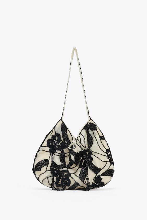 Bílá kabelka s černou květinovou výšivkou a tenkým uchem.