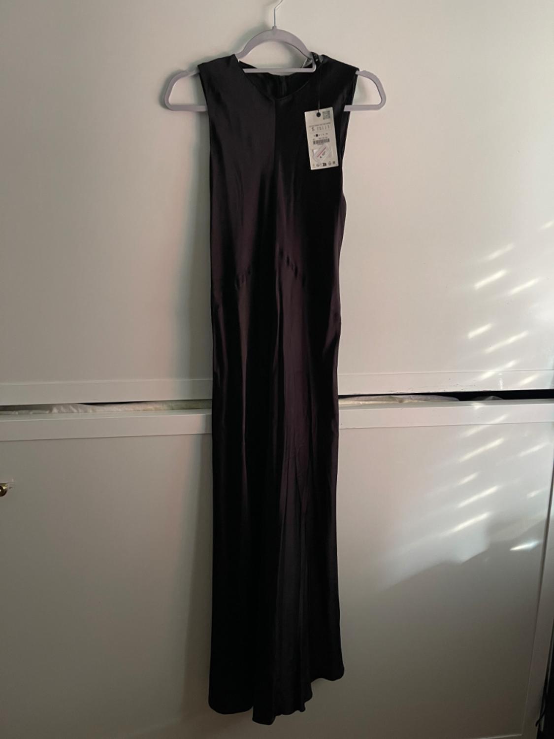Long black sleeveless dress hanging on a white hanger, with visible tag. White background with soft shadows.