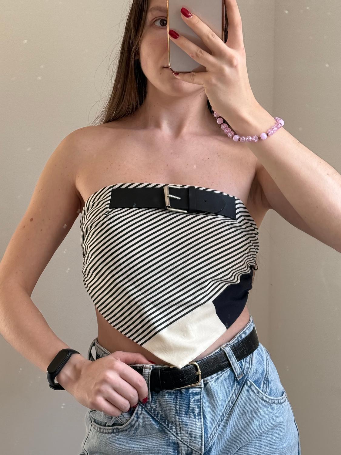 Woman in a black and white striped top with a belt, high-waisted jeans, a pink bracelet, and red nails, taking a selfie in a mirror.