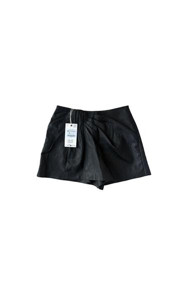 Black shorts with a draped detail at the front on a white background. Label with the text “XS US $49 UK £29”.