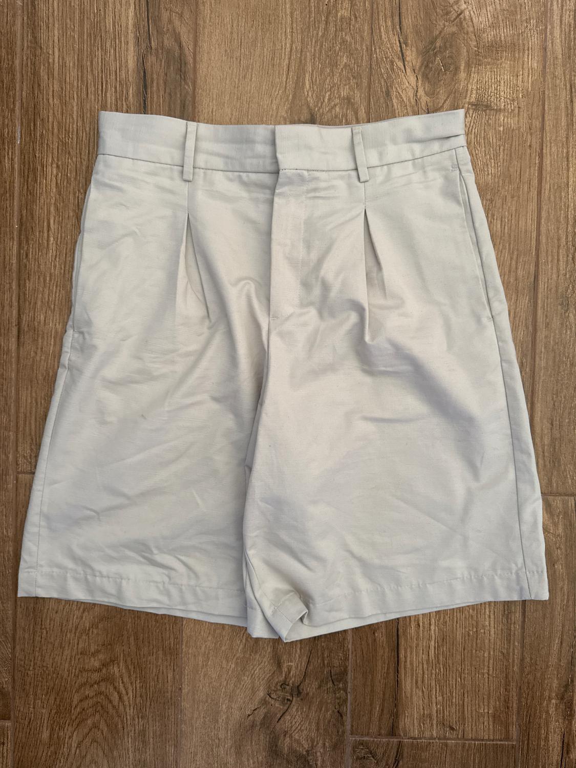 Beige shorts with front pleats and belt loops, on a brown wooden floor.