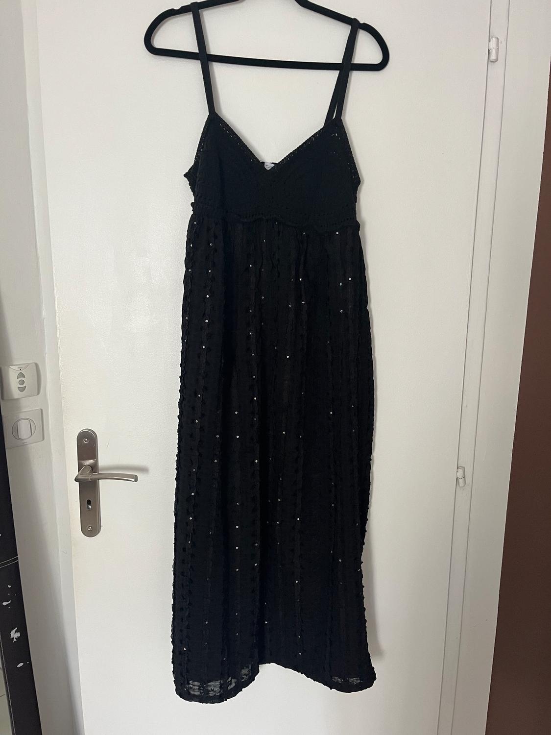 Black dress with thin straps and sparkly details hanging on a hanger over a white door.