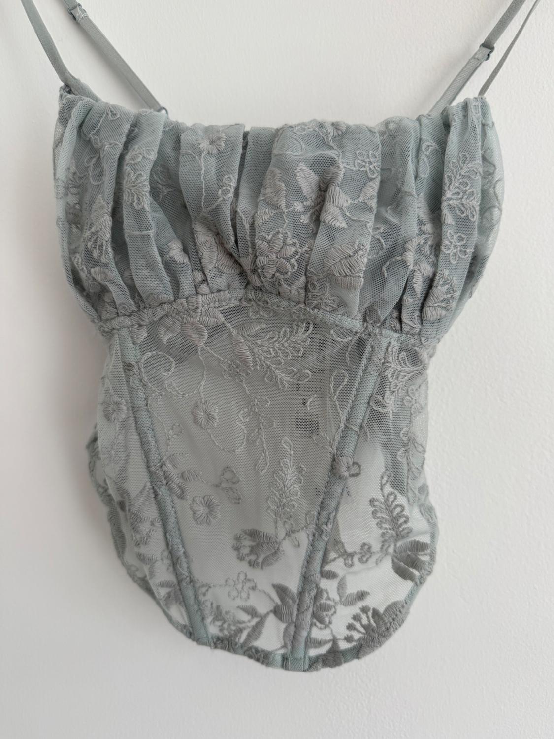 Grey lace top with spaghetti straps and floral design hanging on a white wall.