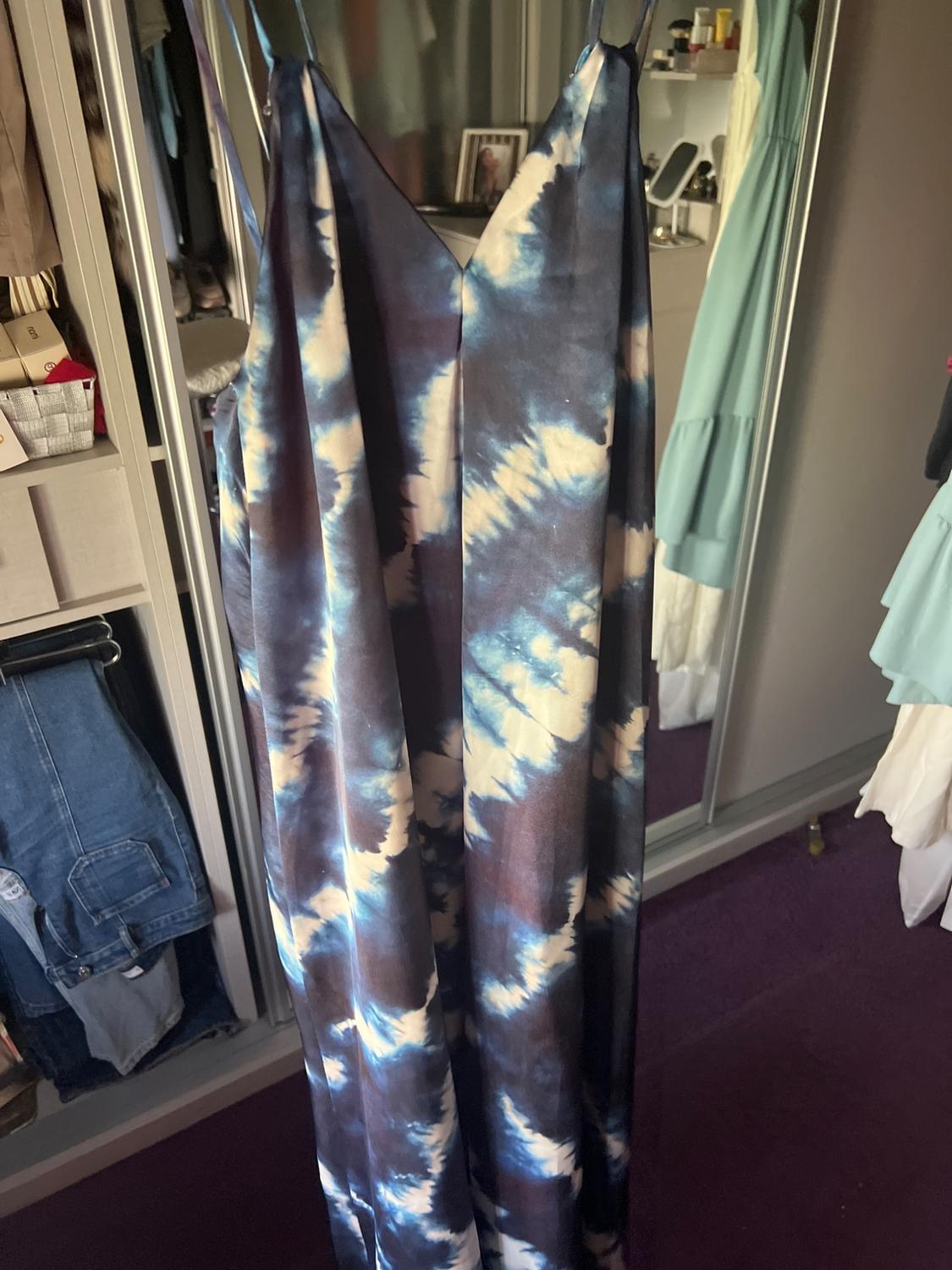 Blue and white tie-dye maxi dress with straps, hanging in front of a mirrored wardrobe in a room with a purple carpet.