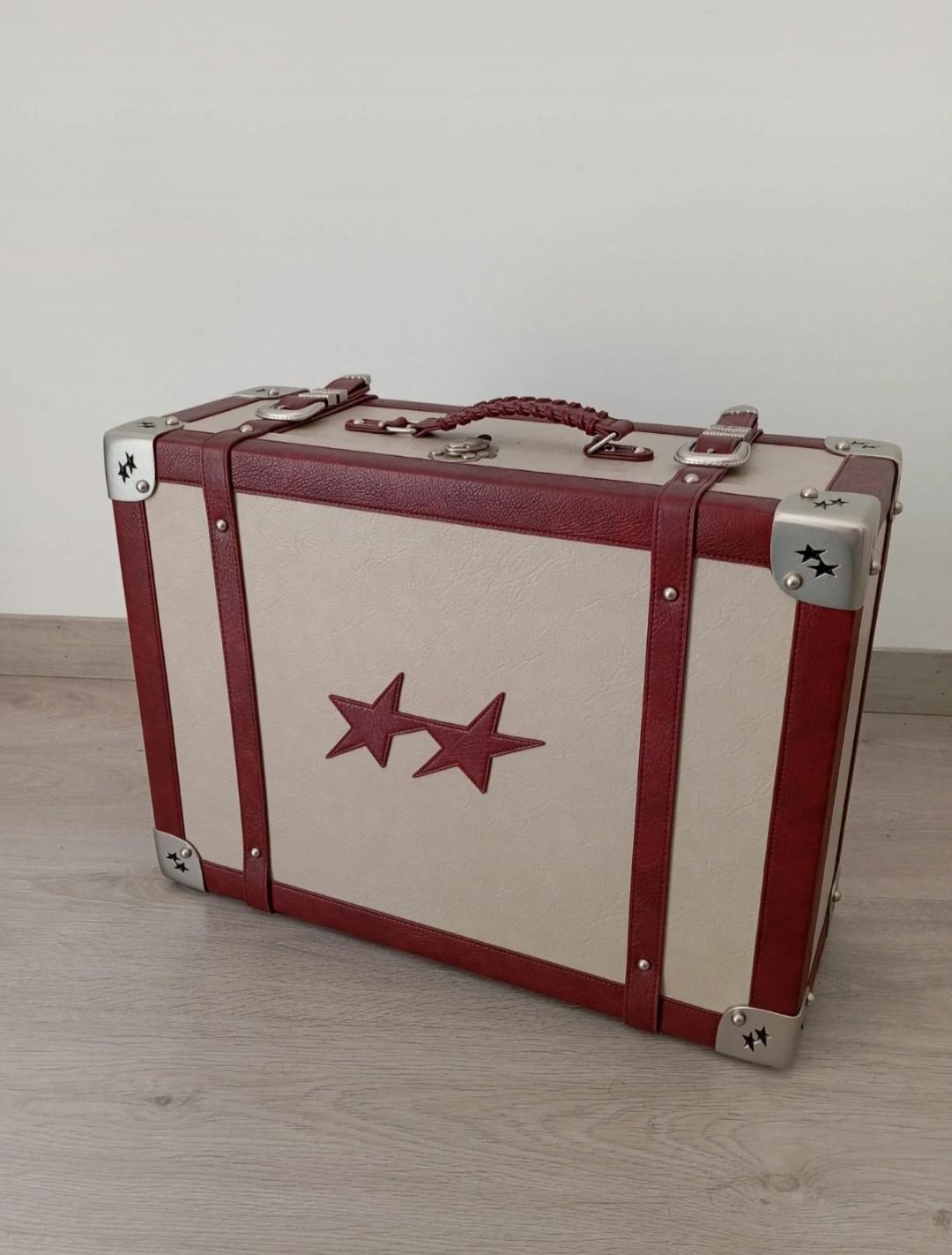 Vintage beige suitcase with red accents and stars on the corners and front, on a light wood floor.