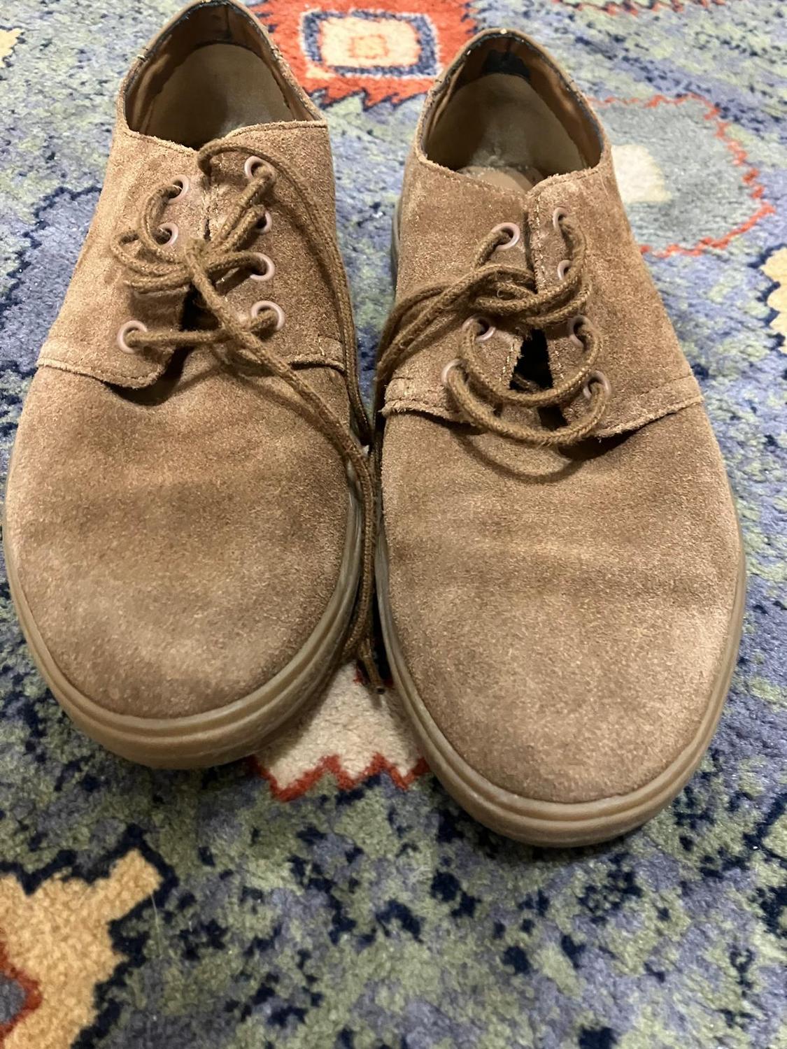 Brown suede shoes with laces on a colourful rug with geometric patterns in shades of blue and orange.