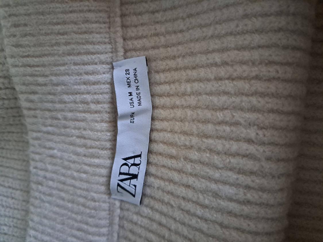 White clothing label with text: "ZARA, EUR M, USA M, MEX 28, MADE IN CHINA" on beige knit fabric.