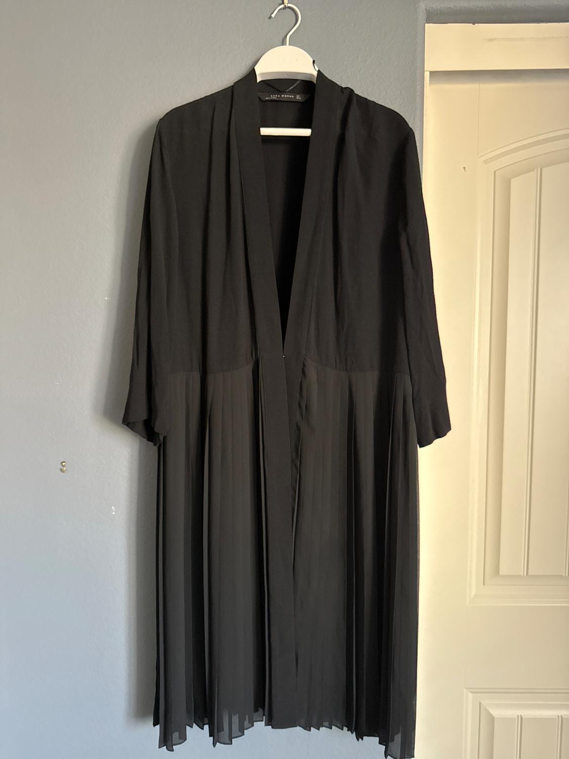 Front view of a black dress with pleats and three-quarter sleeves hanging on a hanger.