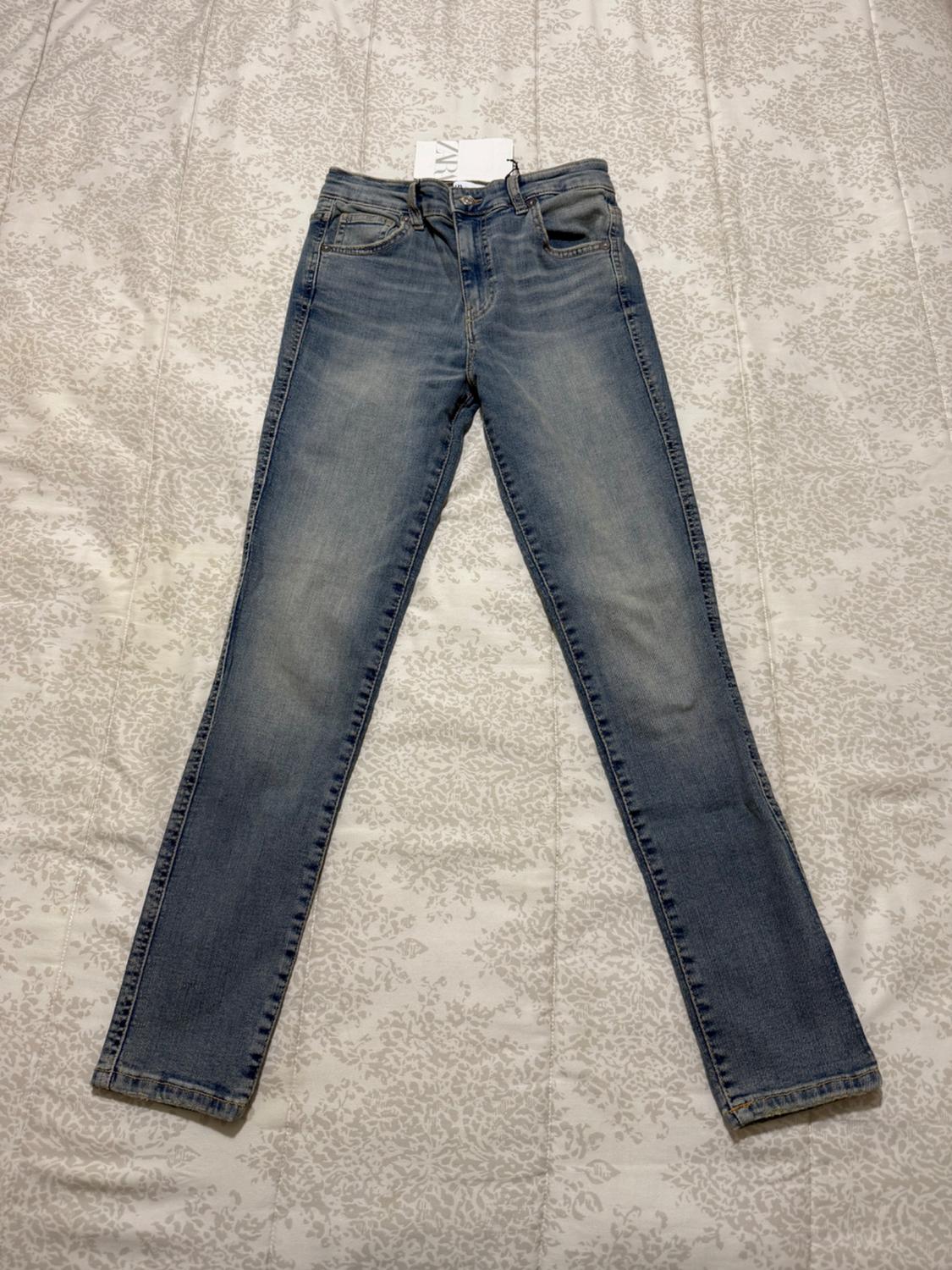 Light blue jeans on a grey floral patterned quilt. Visible label on the waistband.