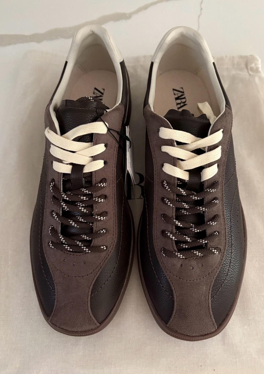 Brown sneakers with white, speckled laces on a light-colored canvas bag. ZARA text on the insoles.