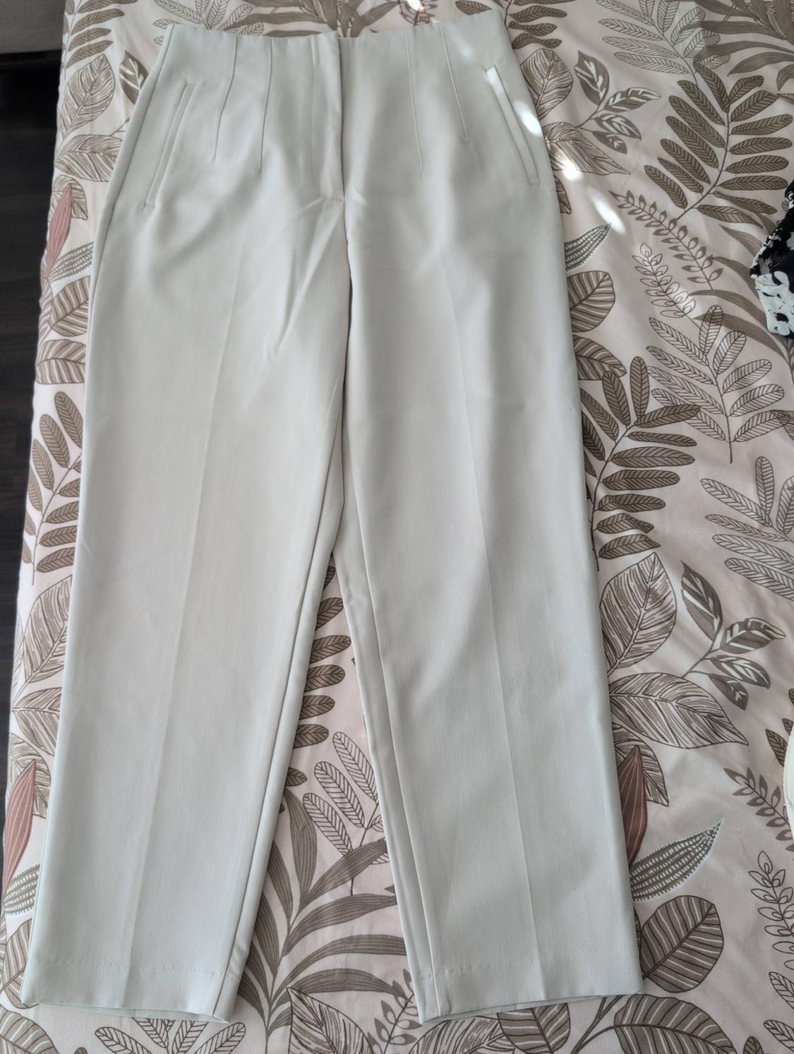 Light tailored trousers with pleats and a front crease, laid out on a fabric with a neutral-toned leaf print.