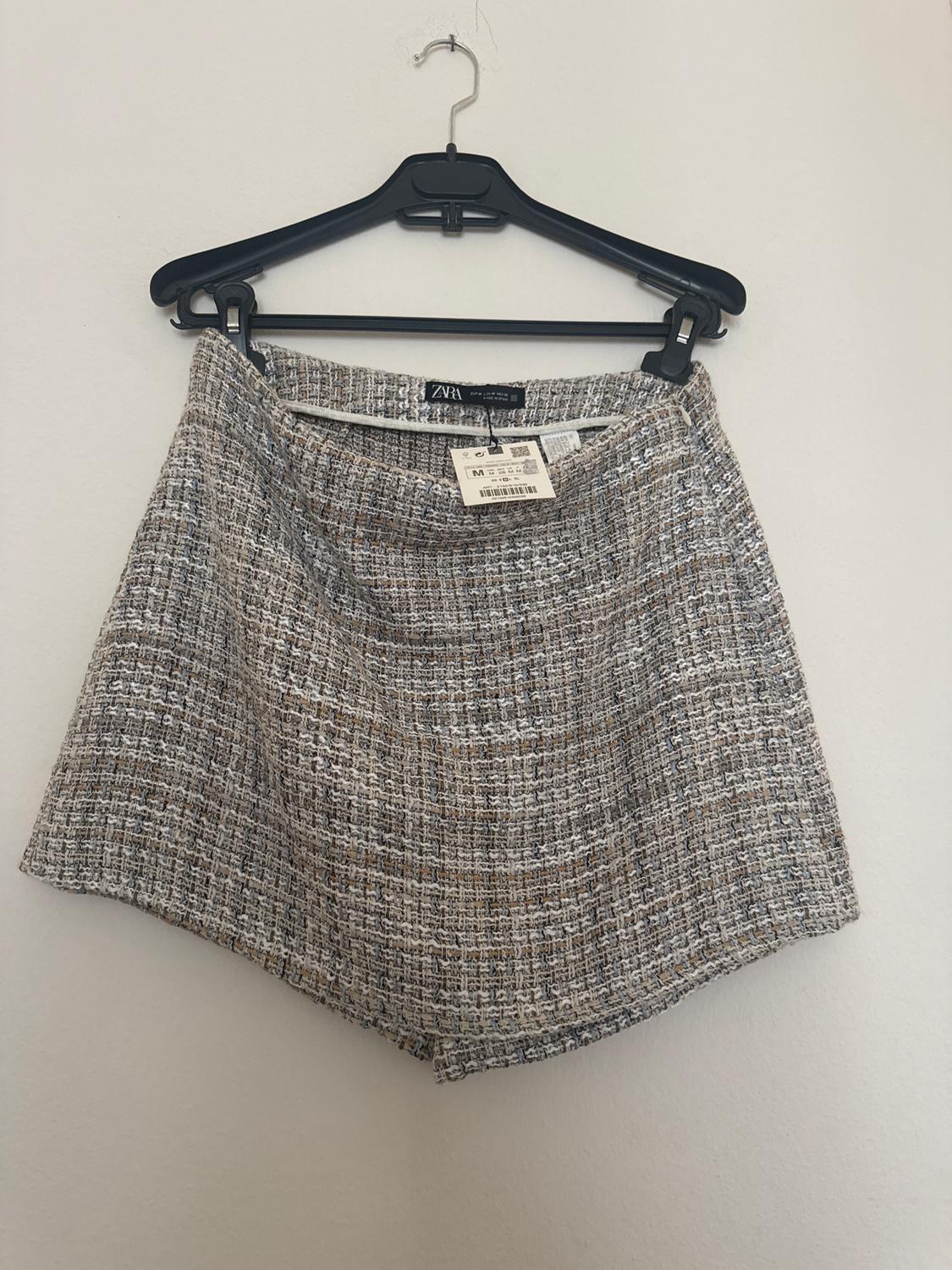 Textured fabric shorts in shades of grey and brown hanging on a black hanger. Visible label with size and price details.