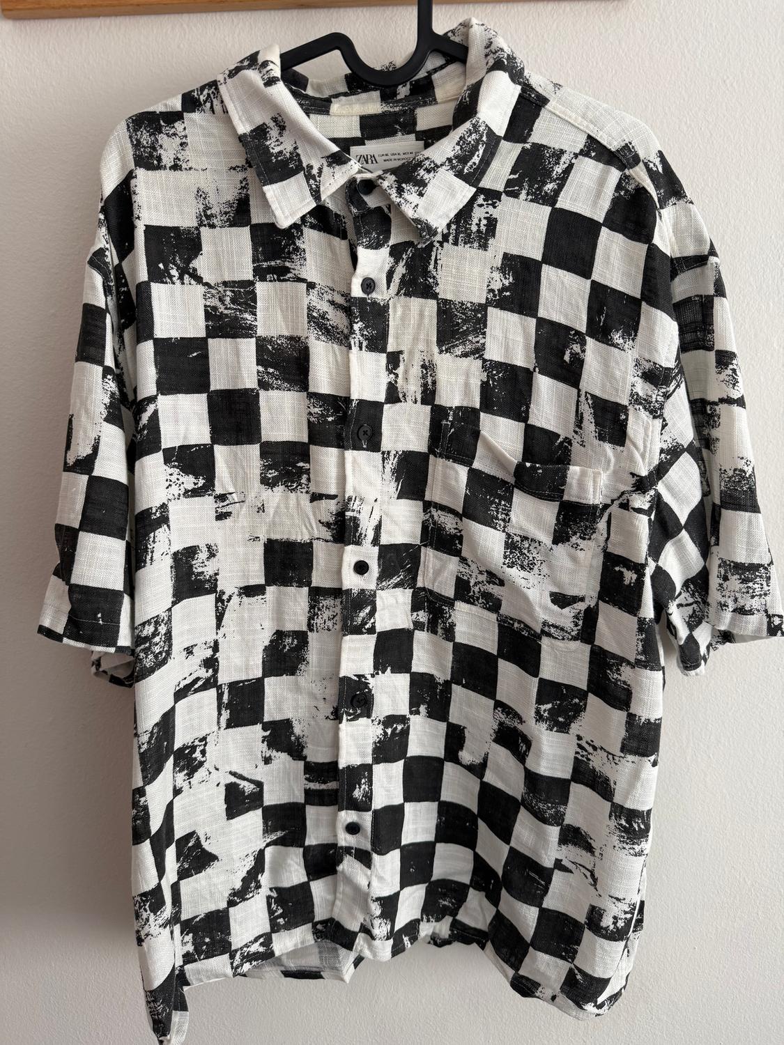 Black and white checked shirt with a distressed effect, hanging on a black hanger against a white wall.