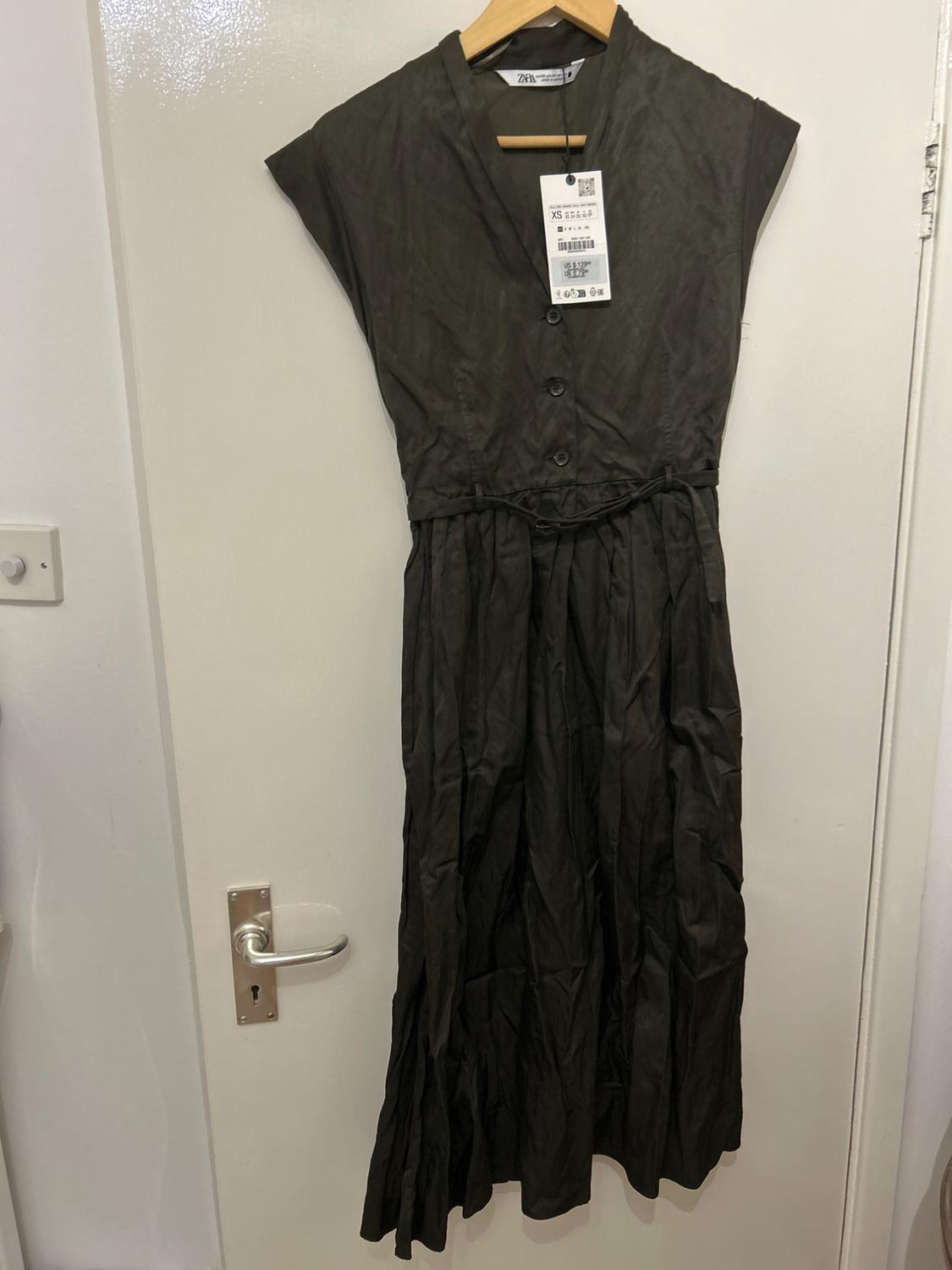Sleeveless black dress hanging on a white door, with front buttons and visible XS size tag.