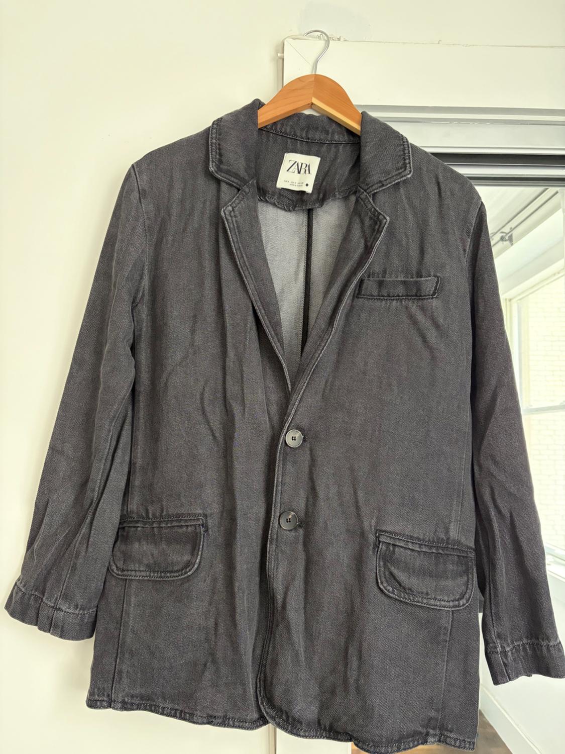 Dark grey casual blazer jacket hanging on a wooden hanger against a white background. Interior label with the text ZARA.