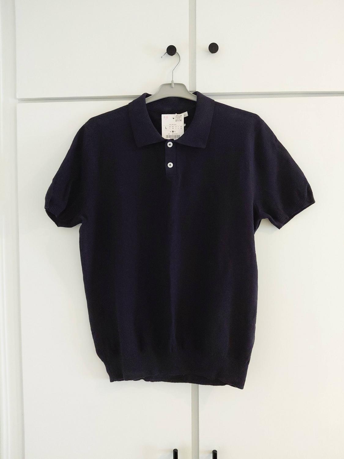 Navy blue short-sleeved polo shirt with buttons, hanging on a hanger above a white wardrobe with black handles.