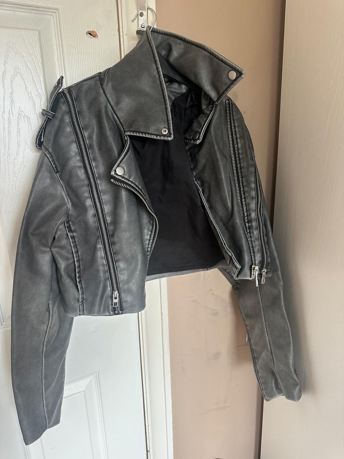 Grey leather jacket hanging on a white door. Short design with zips and large lapels. Casual and modern vibe.