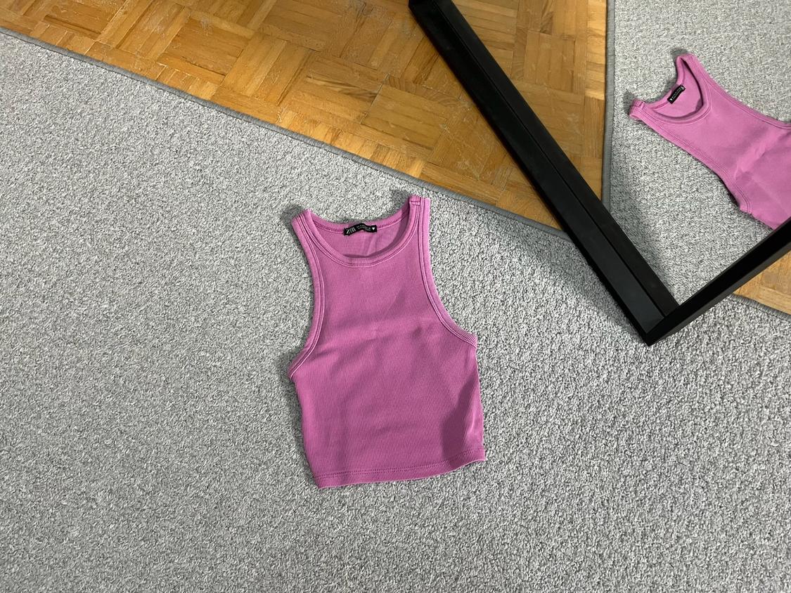 Pink ribbed crop top on a grey rug. A mirror with a black frame reflects the garment and the wooden floor.