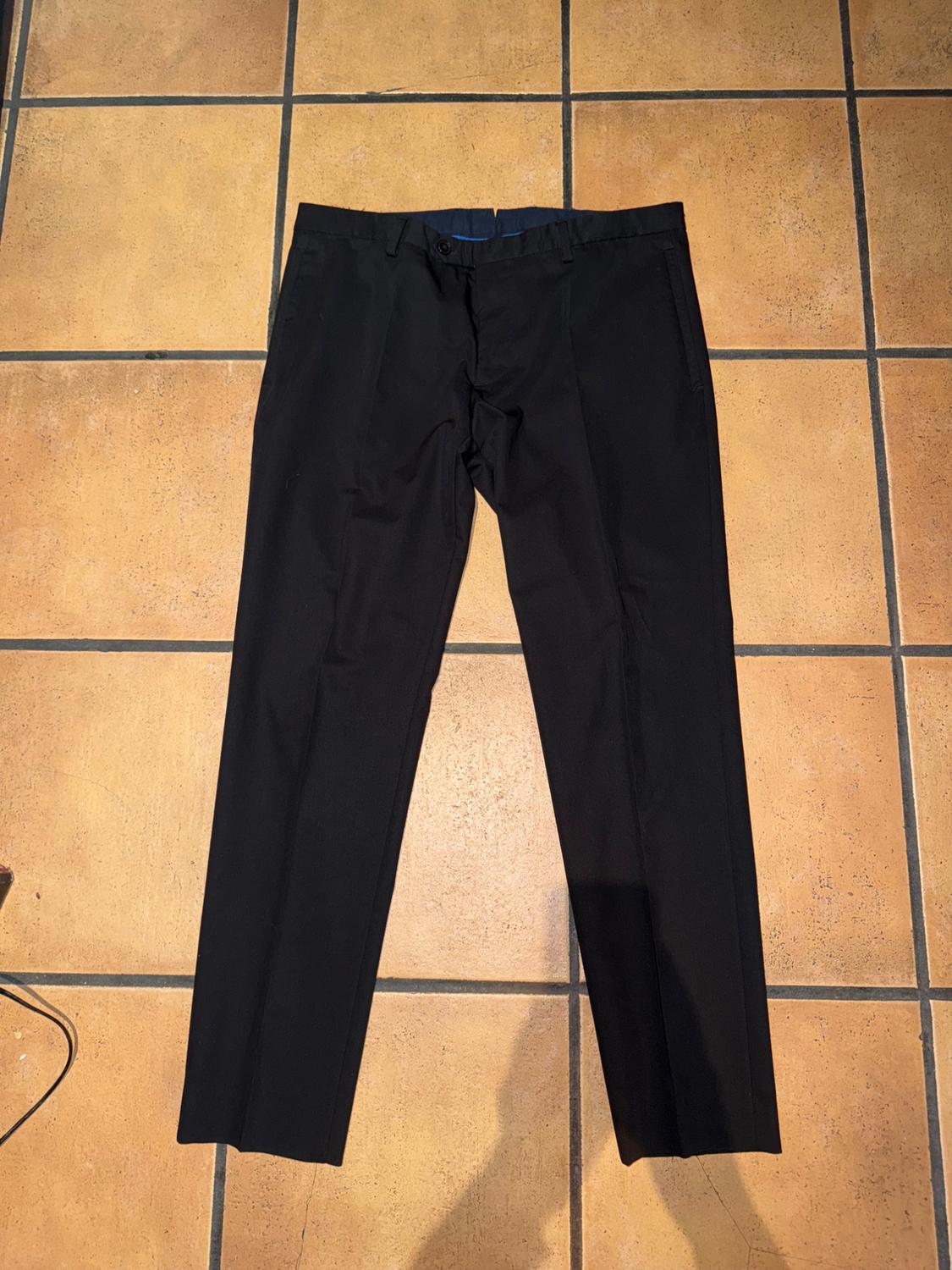 Black dress trousers on a brown tiled floor. Light creates shadows on the floor.