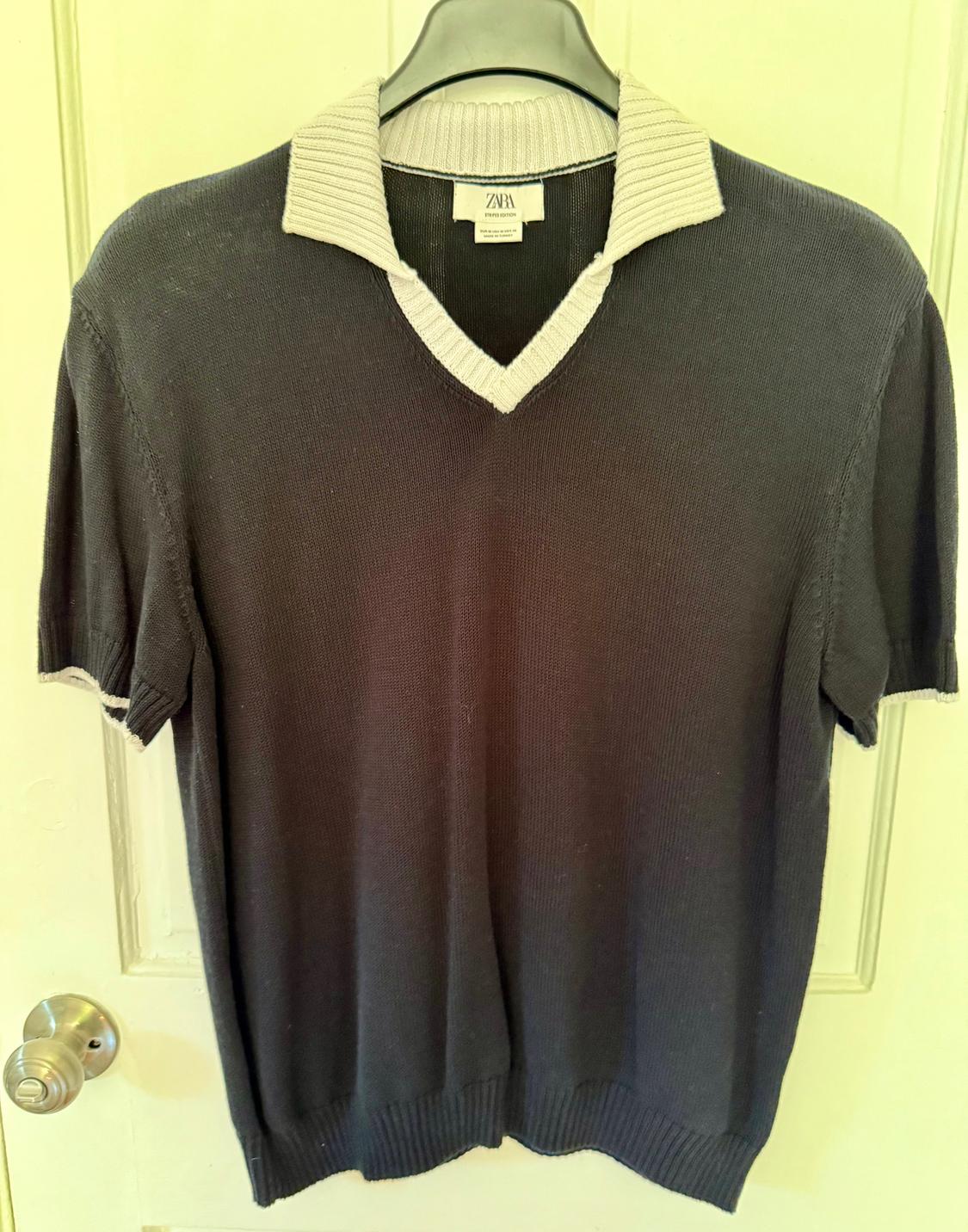 Grey short-sleeved V-neck sweater with white trim, hanging on a hanger. Visible label with text: "Zara".