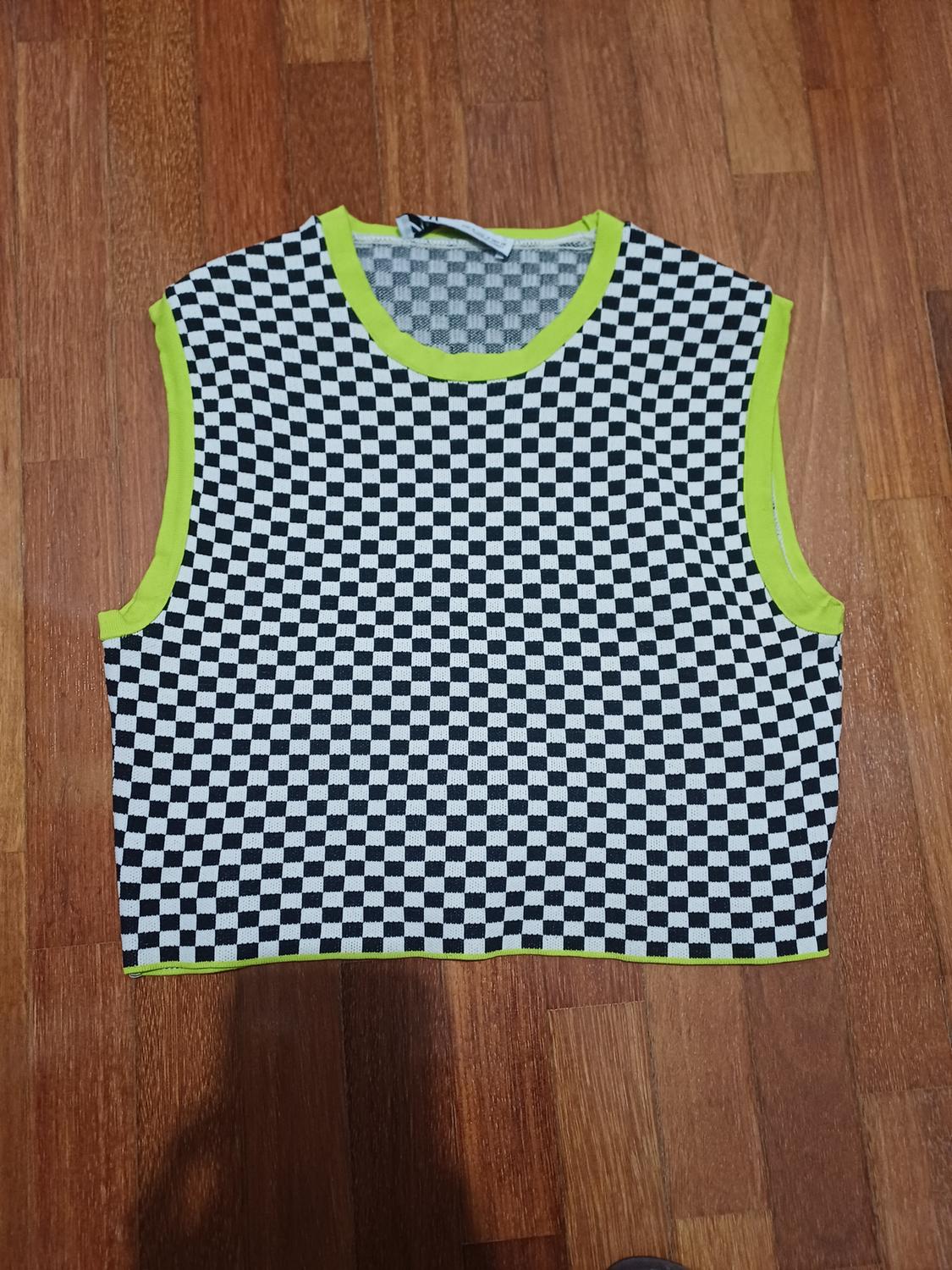 Cropped sleeveless top with a black-and-white check pattern and neon-green trims, on a wooden floor.