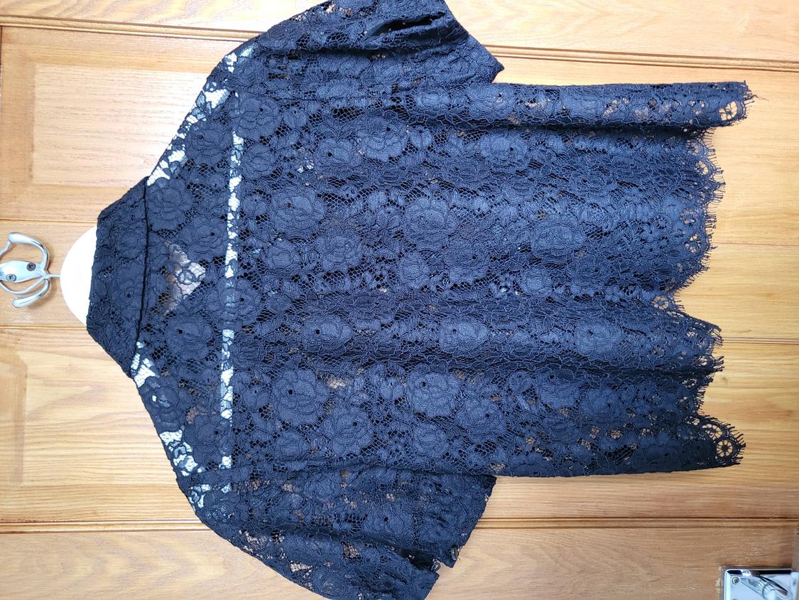 Black lace blouse hanging on a wooden door. Floral design with sheer panels and short sleeves.