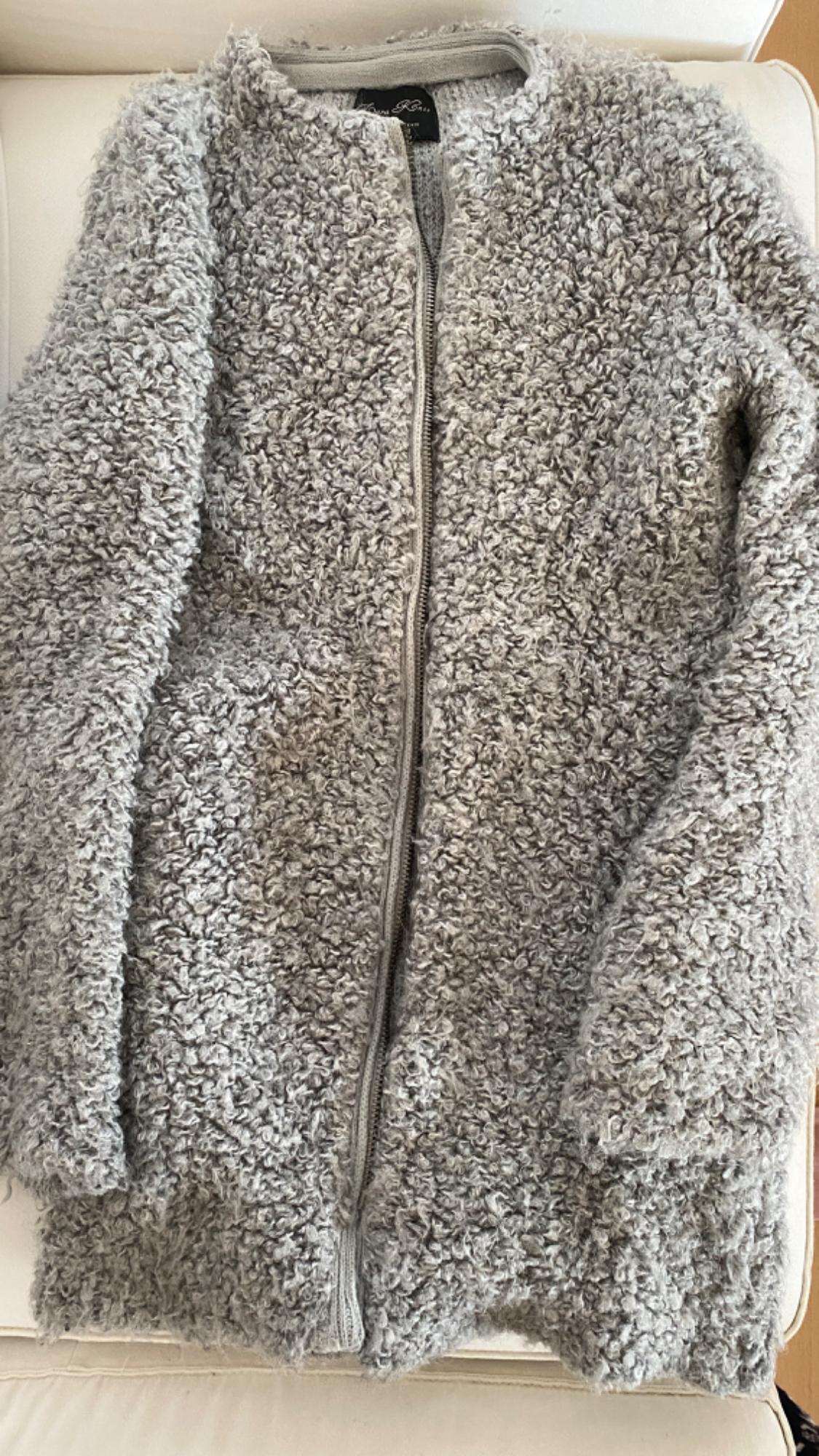 Fluffy grey zip-up jacket, placed on a white sofa. Visible tag on the collar.