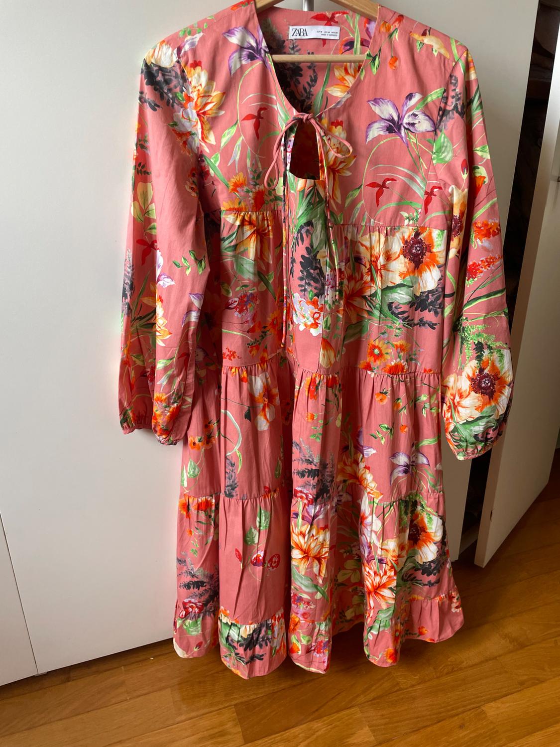 Front view of a multicoloured floral print dress with a bow at the neckline and long puffed sleeves.
