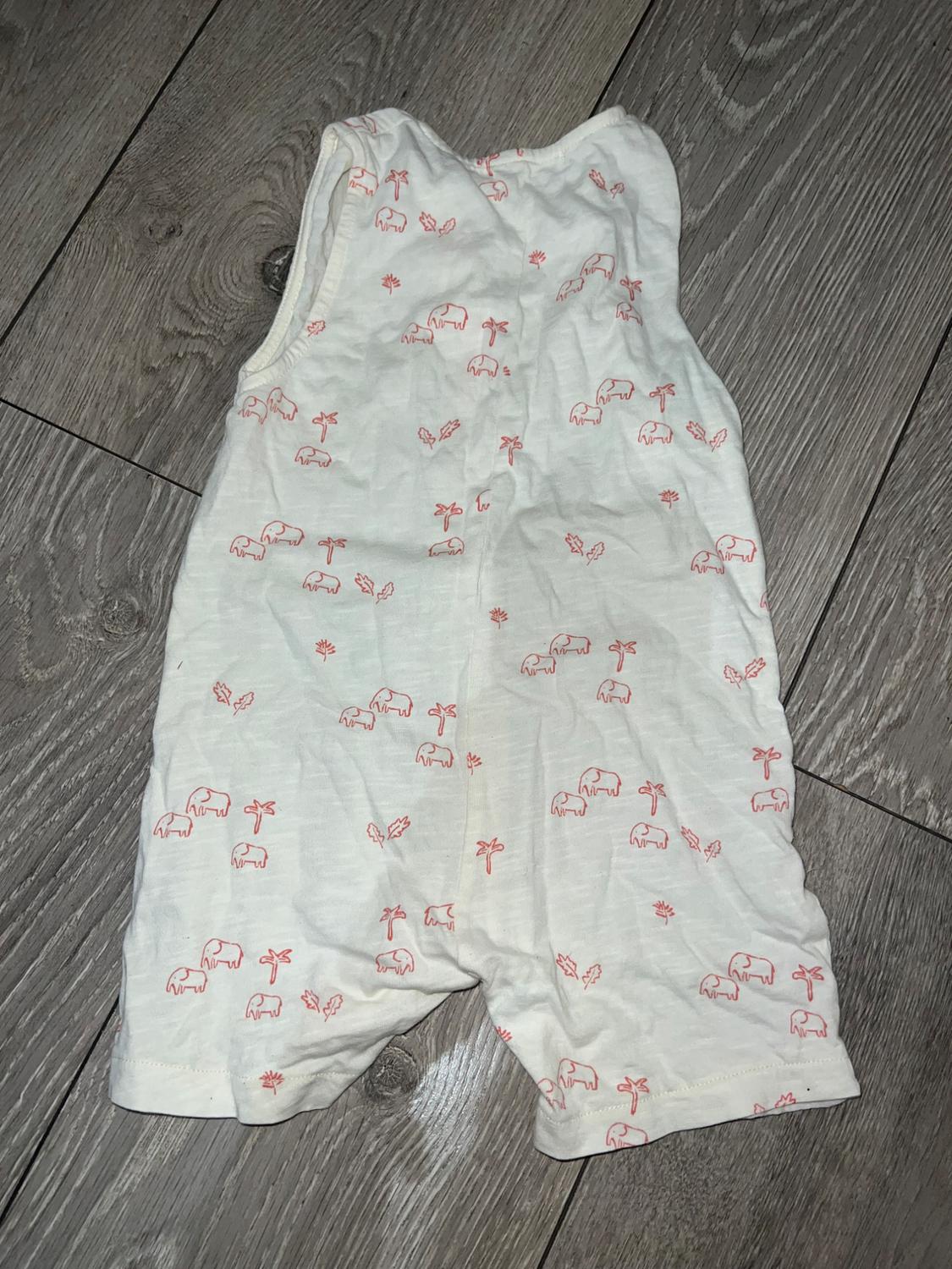 Children's white pyjamas with elephant and palm tree print in red, on grey wooden floor.