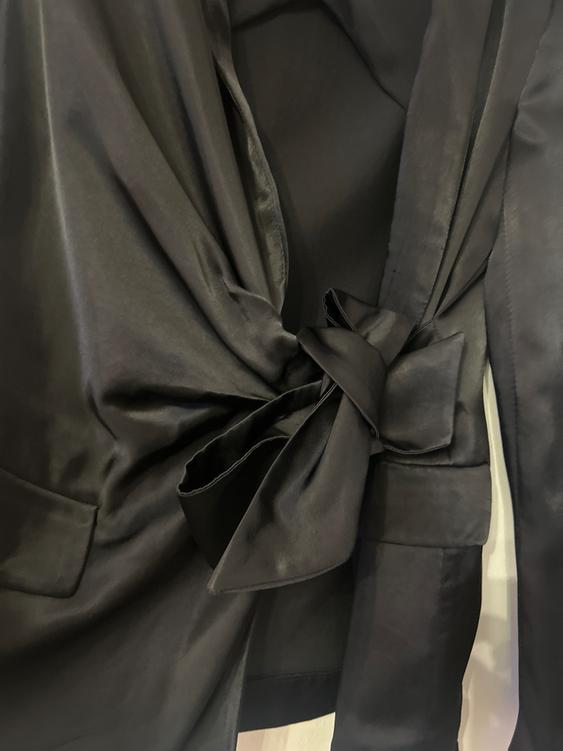 Close-up of a black jacket with a large bow on the front, showing details of the satin fabric.