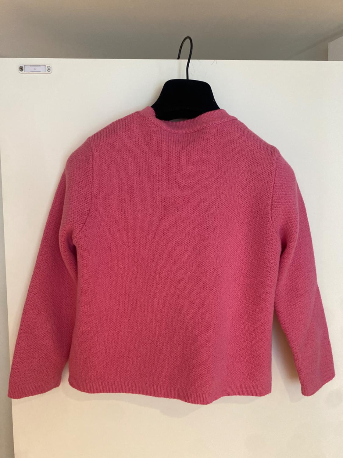 Pink long-sleeved knitted jumper hanging on a black hanger over a white door. Back view.