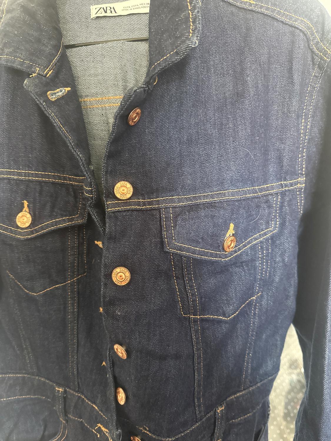 Blue denim jacket with gold metal buttons and visible stitching. Visible internal label with text "ZARA".