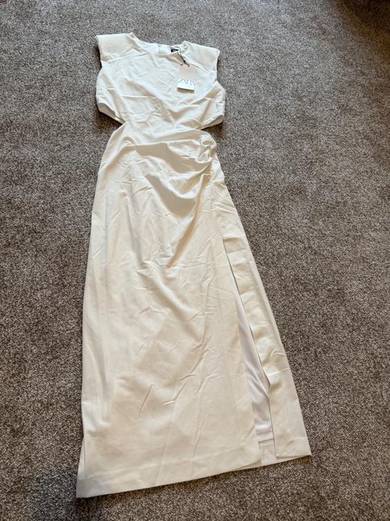 White sleeveless maxi dress on a grey carpet, with a visible label on the collar.